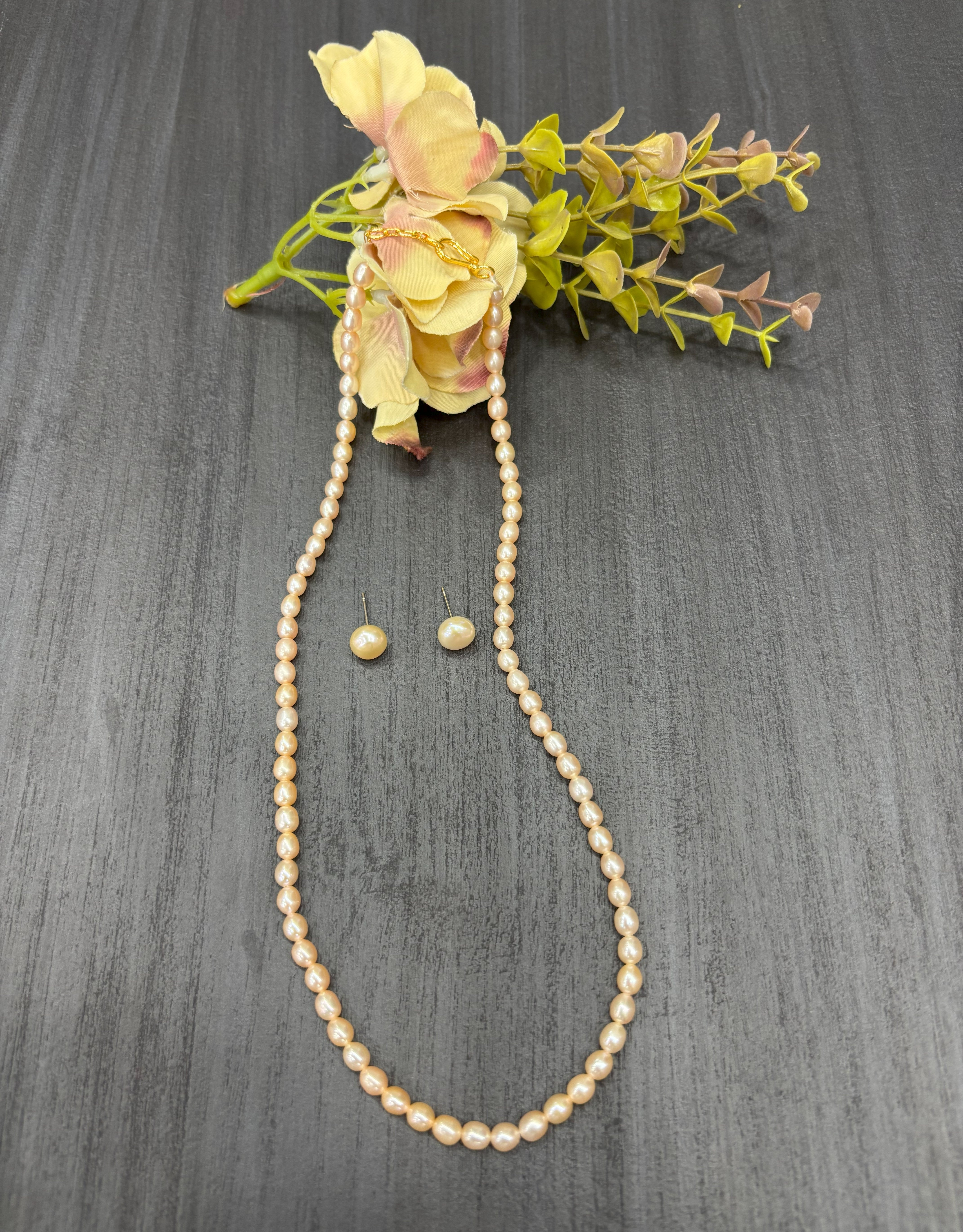 Pearl necklace and earrings with flowers on a gray surface