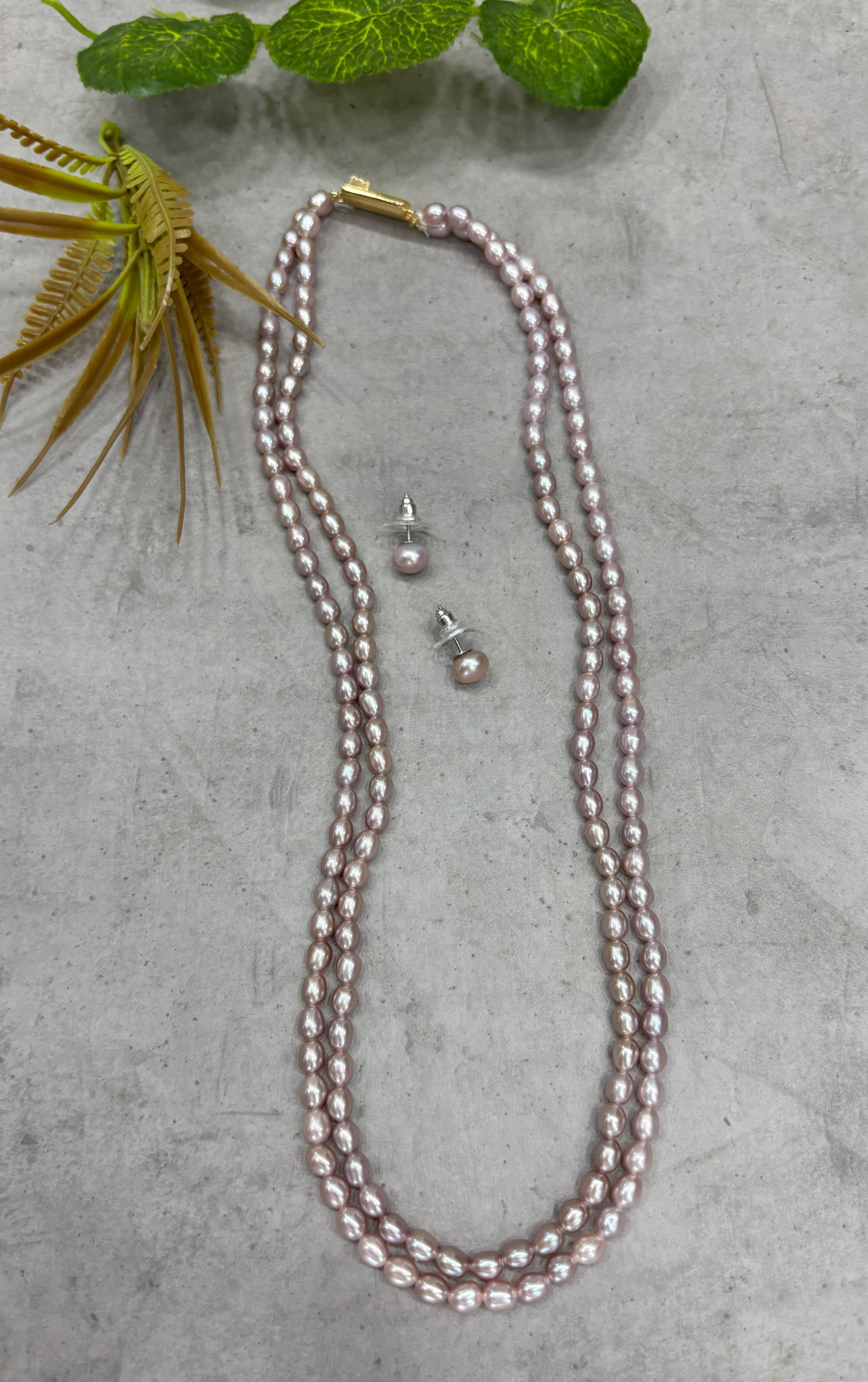Pearl necklace and earrings for women on gray surface with green leaves